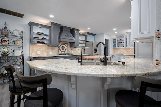 kitchen featuring a kitchen breakfast bar, appliances with stainless steel finishes, custom exhaust hood, sink, and gray cabinets