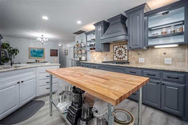 kitchen featuring stainless steel gas stovetop, custom exhaust hood, light stone countertops, and decorative backsplash