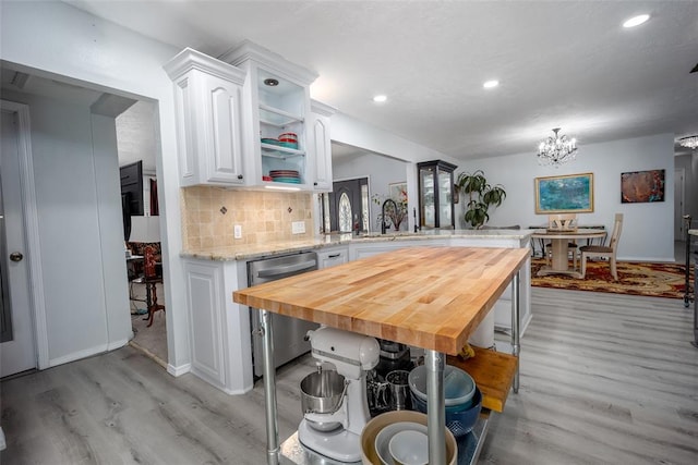 kitchen featuring kitchen peninsula, stainless steel dishwasher, white cabinetry, decorative backsplash, and wood counters