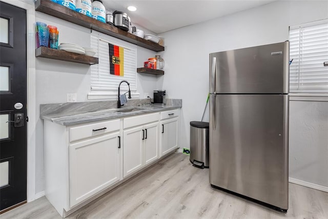 kitchen with light stone countertops, white cabinets, sink, light hardwood / wood-style flooring, and stainless steel fridge