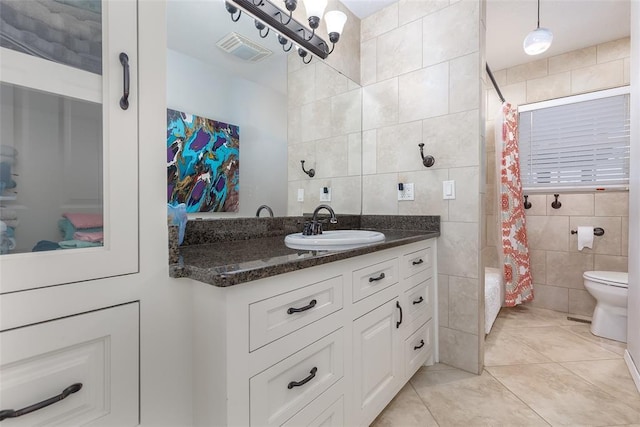 bathroom with toilet, tile patterned flooring, vanity, and tile walls