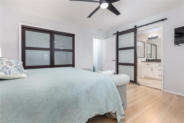 bedroom featuring ceiling fan, a barn door, light hardwood / wood-style floors, and ensuite bath