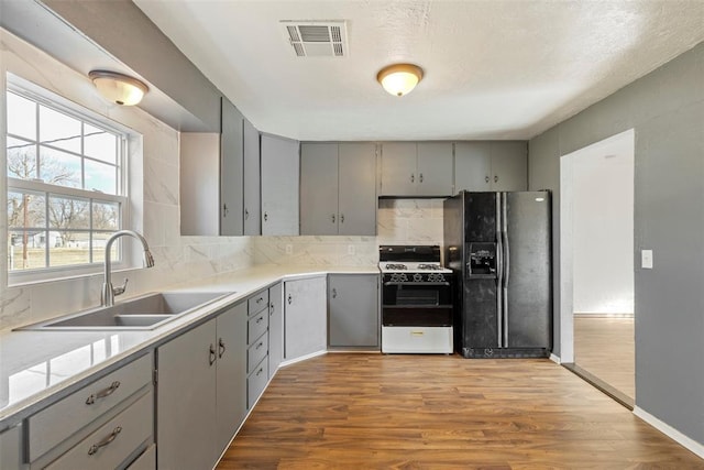 kitchen featuring gray cabinets, sink, white range with gas cooktop, light wood-type flooring, and black fridge with ice dispenser