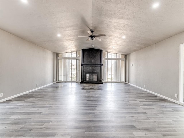 unfurnished living room with ceiling fan, light hardwood / wood-style flooring, lofted ceiling, and a fireplace