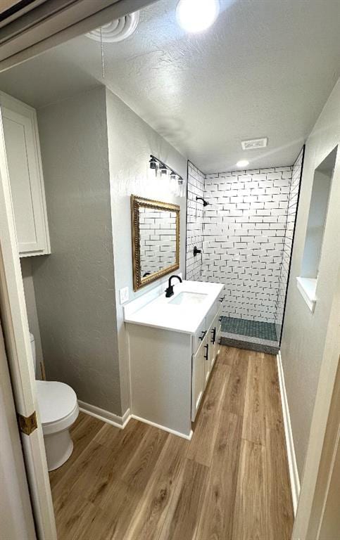 bathroom with a textured ceiling, vanity, toilet, hardwood / wood-style flooring, and tiled shower