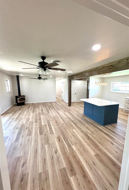 unfurnished living room with light wood-type flooring, ceiling fan, and a wood stove