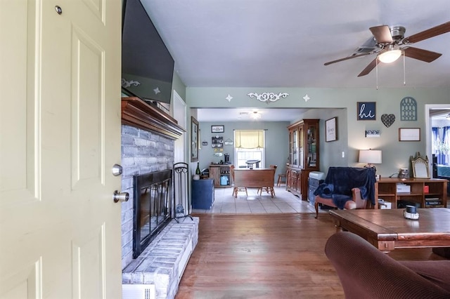 living room featuring ceiling fan, light hardwood / wood-style floors, and a brick fireplace