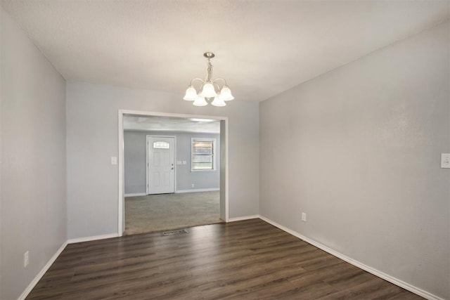 empty room with dark hardwood / wood-style floors and a chandelier