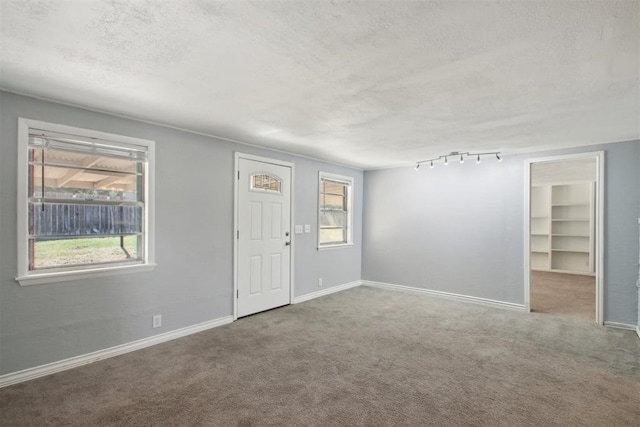 carpeted empty room with a textured ceiling, track lighting, and plenty of natural light