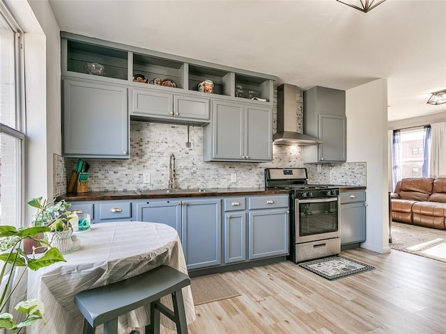 kitchen with stainless steel gas range, wall chimney exhaust hood, light hardwood / wood-style floors, sink, and decorative backsplash