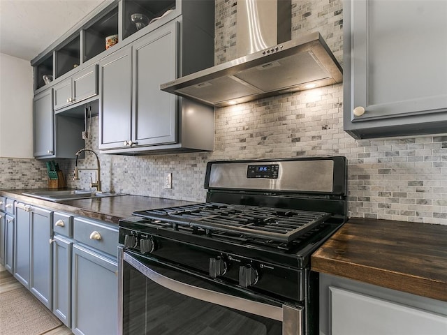 kitchen featuring wood counters, wall chimney range hood, tasteful backsplash, stainless steel gas stove, and sink