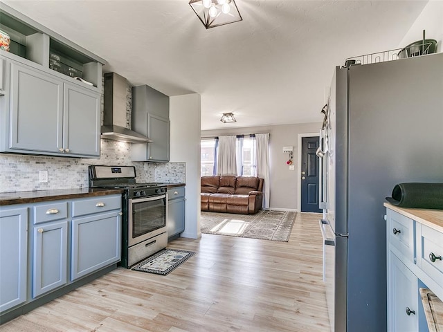 kitchen with wall chimney range hood, backsplash, appliances with stainless steel finishes, and light wood-type flooring