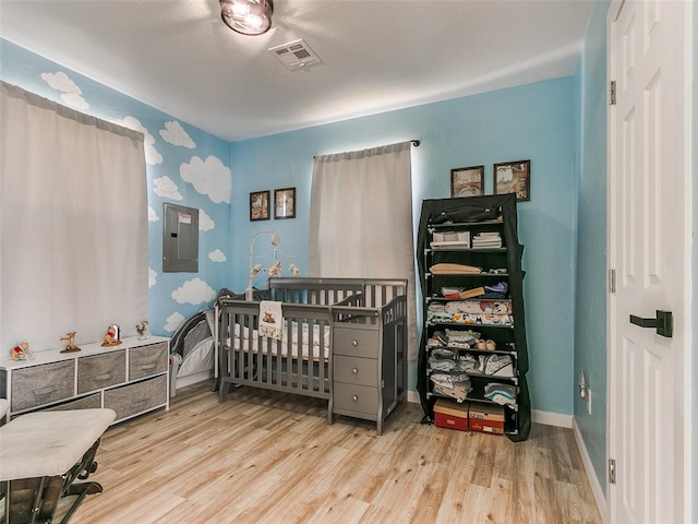 bedroom with light hardwood / wood-style flooring, electric panel, and a crib