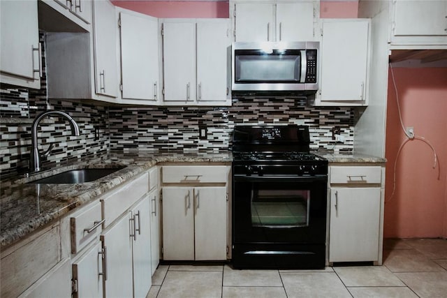 kitchen featuring black gas range oven, light tile patterned flooring, stone counters, white cabinets, and sink