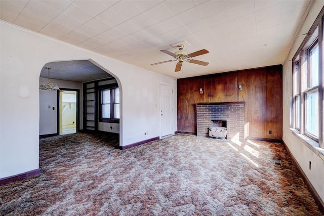 unfurnished living room featuring ceiling fan, a healthy amount of sunlight, a brick fireplace, and wooden walls