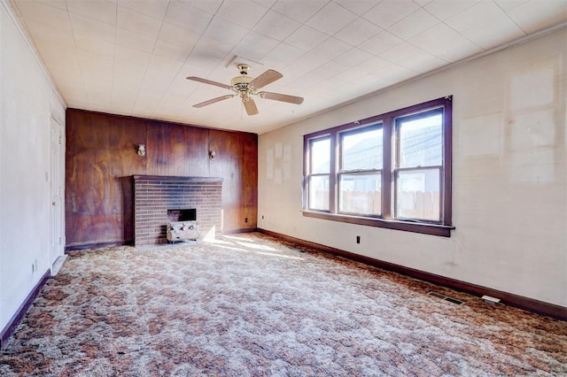 unfurnished living room with ceiling fan, wood walls, carpet flooring, a brick fireplace, and crown molding