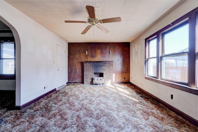 unfurnished living room with ceiling fan, a brick fireplace, wood walls, and dark colored carpet