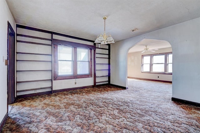 empty room with a textured ceiling, ceiling fan with notable chandelier, and dark carpet