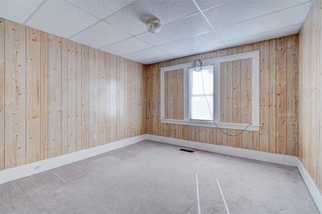 carpeted spare room with a drop ceiling and wood walls