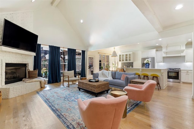 living room with beam ceiling, high vaulted ceiling, a brick fireplace, and light wood-type flooring