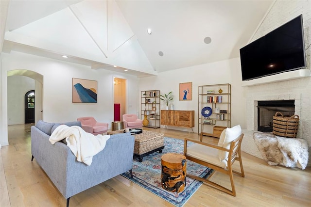 living room featuring high vaulted ceiling, a brick fireplace, and light hardwood / wood-style flooring