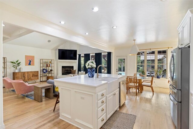 kitchen featuring lofted ceiling with beams, a fireplace, a sink, appliances with stainless steel finishes, and light wood finished floors