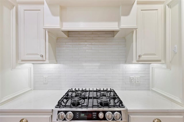 kitchen featuring stainless steel gas range, white cabinets, light stone counters, and tasteful backsplash