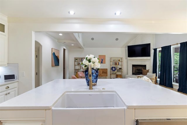 kitchen featuring open floor plan, a large fireplace, an island with sink, and lofted ceiling