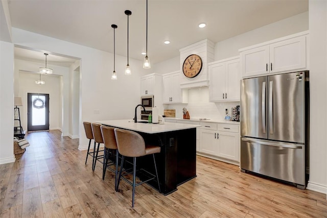 kitchen featuring pendant lighting, an island with sink, white cabinets, black appliances, and light hardwood / wood-style flooring