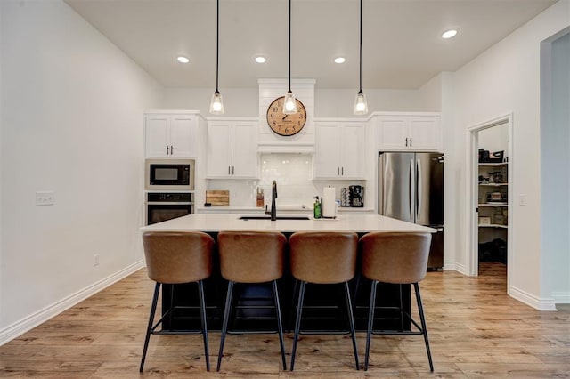 kitchen with appliances with stainless steel finishes, pendant lighting, white cabinetry, an island with sink, and sink