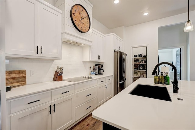 kitchen with sink, stainless steel fridge, white cabinetry, hanging light fixtures, and black electric stovetop