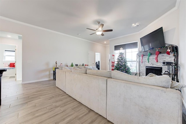 living room featuring ceiling fan, ornamental molding, and a stone fireplace