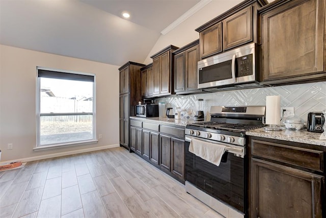 kitchen with appliances with stainless steel finishes, lofted ceiling, backsplash, light stone counters, and dark brown cabinets