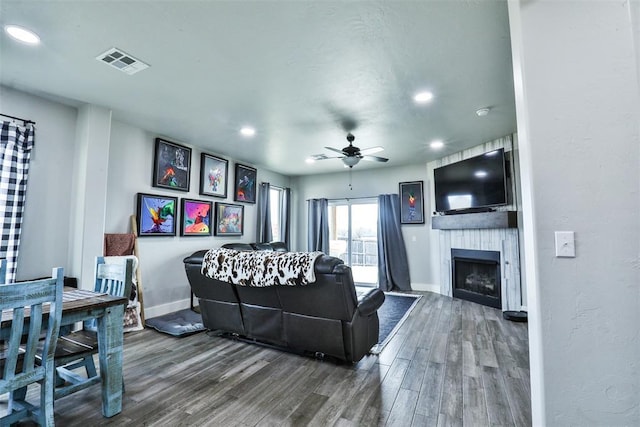 living room featuring wood-type flooring, a large fireplace, and ceiling fan