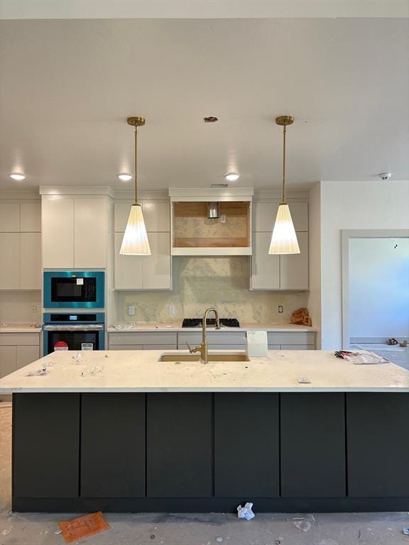 kitchen featuring pendant lighting, stainless steel oven, a center island with sink, and gray cabinetry