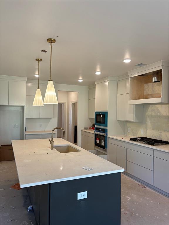 kitchen featuring stainless steel appliances, pendant lighting, sink, and a center island with sink