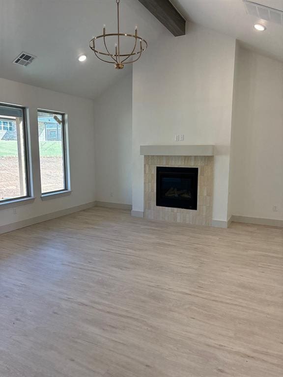 unfurnished living room with light hardwood / wood-style flooring, lofted ceiling with beams, a tile fireplace, and a chandelier