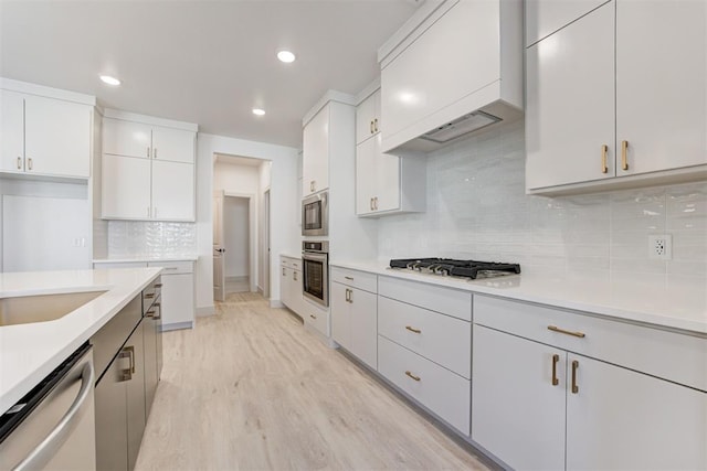 kitchen with light hardwood / wood-style flooring, premium range hood, white cabinetry, appliances with stainless steel finishes, and decorative backsplash