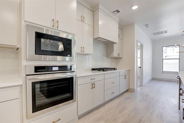 kitchen with white cabinetry, appliances with stainless steel finishes, light wood-type flooring, and decorative backsplash