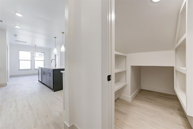 corridor with sink, built in features, and light wood-type flooring