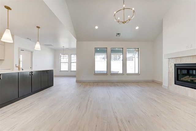 unfurnished living room with a notable chandelier, vaulted ceiling, a tile fireplace, and light wood-type flooring