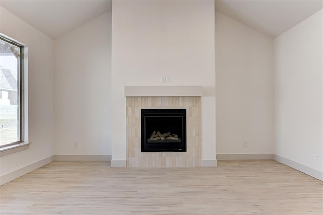 unfurnished living room featuring a tiled fireplace, vaulted ceiling, and light wood-type flooring