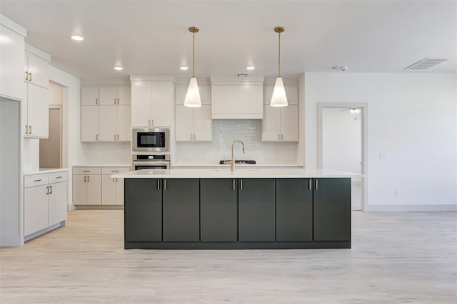 kitchen with built in microwave, oven, hanging light fixtures, and a center island with sink