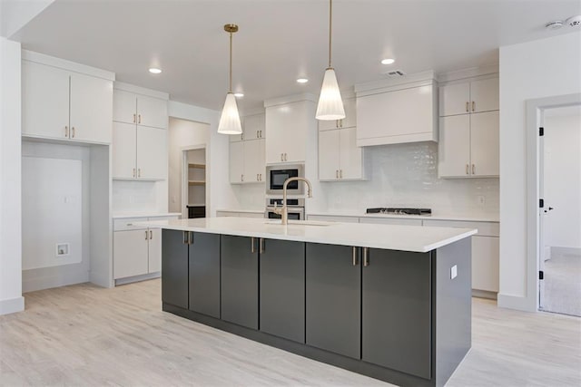 kitchen with built in microwave, pendant lighting, an island with sink, and white cabinets