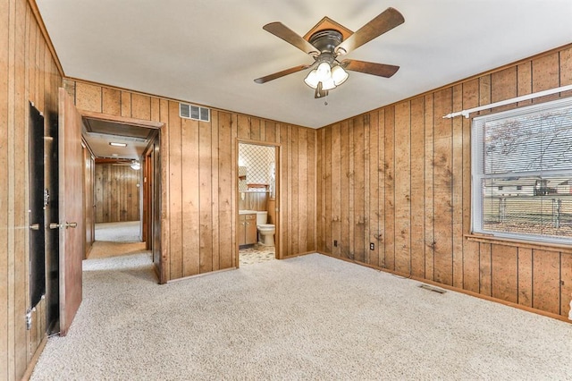 unfurnished bedroom featuring light carpet, wooden walls, connected bathroom, and ceiling fan