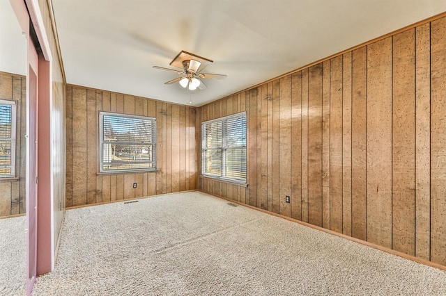 spare room featuring carpet floors, wooden walls, and ceiling fan