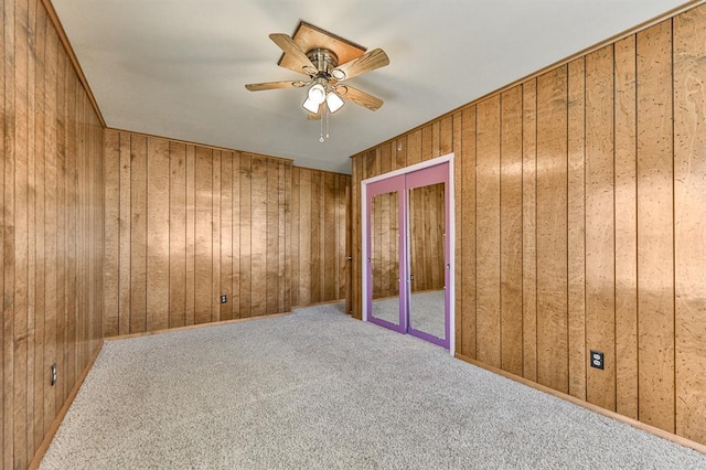 unfurnished bedroom with carpet floors, ceiling fan, and wood walls