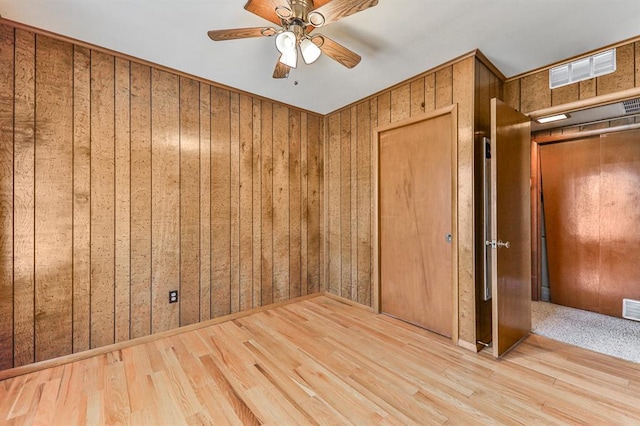 empty room featuring ceiling fan, light wood-type flooring, and wooden walls