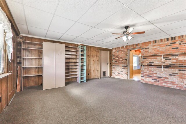 unfurnished living room featuring brick wall, carpet floors, a paneled ceiling, and wooden walls