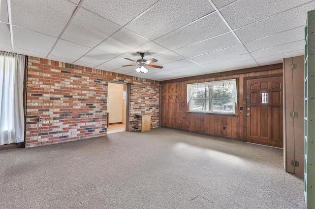 unfurnished living room featuring a paneled ceiling, wooden walls, and brick wall